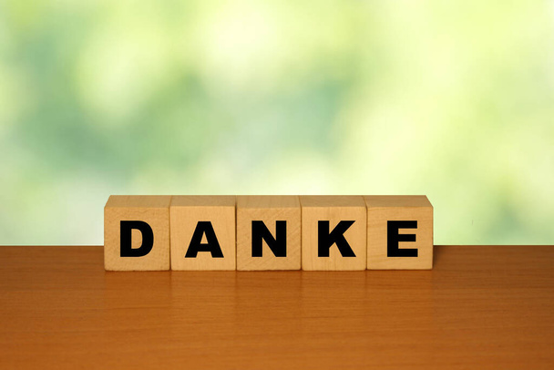 Слово с надписью DANKE на деревянном столе на кубических блоках с зеленым бэкграундом природы
 - Фото, изображение