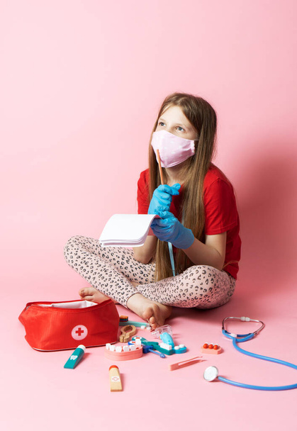 Personal protective equipment: a teenager girl in a medical mask and blue gloves plays a nurse and holds a stethoscope. - Photo, Image