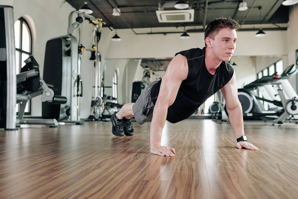 Fit sweaty sportsman standing in plank position in gym to strengthen core muscles - Photo, Image