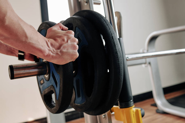 Sporcunun spor salonunda egzersiz yapmadan önce halterlere ağırlık koyduğu yakın plan görüntüsü. - Fotoğraf, Görsel