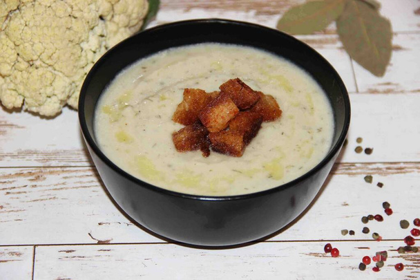 Cauliflower cream soup with croutons, drizzled with olive oil, in a black Cup - Photo, Image
