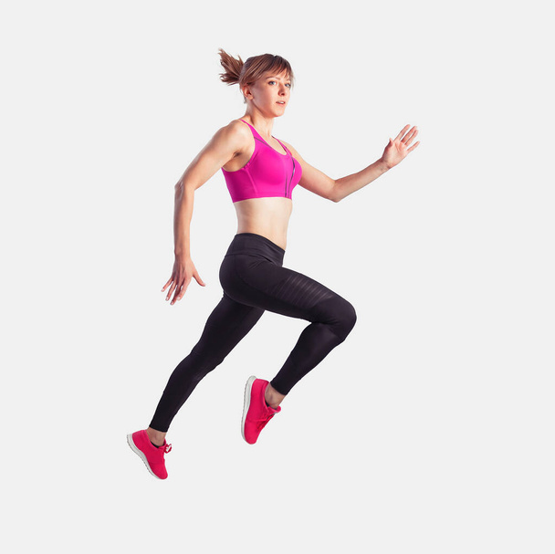Жінка стрибає або біжить у рожевих змійках і зверху, темні легінси на сірому фоні. Динамічний рух. Вид збоку
 - Фото, зображення