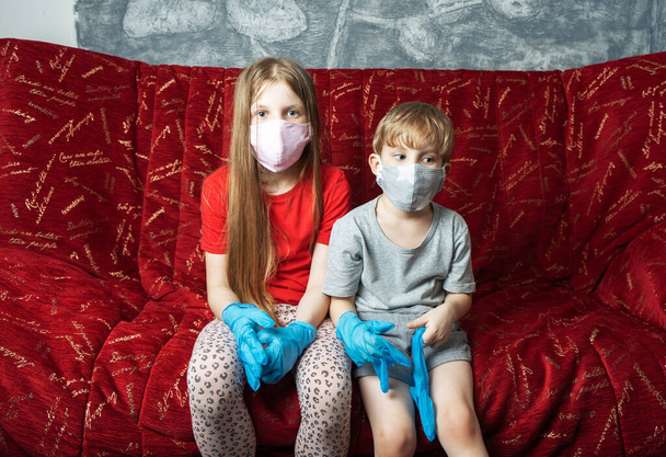 Stay at home: a boy and a girl in a medical mask and gloves are sitting at home on the couch. - Foto, imagen