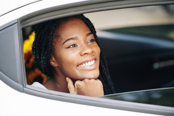 Лицо счастливой красивой черной женщины с белой зубастой улыбкой, смотрящей в окно машины и наслаждающейся поездкой
 - Фото, изображение