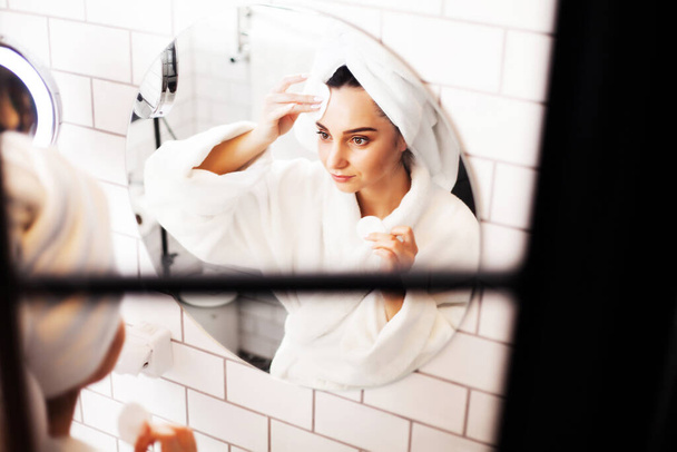 Красивая женщина делает косметические процедуры по уходу за кожей лица в ванной комнате
 - Фото, изображение