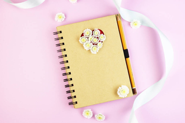 Κάτοψη γραφείου με σημειωματάριο, στυλό και αντίγραφο χώρου σε φόντο παστέλ χρωμάτων. σημειωματάριο με μολύβι και διακοσμητική κορδέλα σε ροζ φόντο - Φωτογραφία, εικόνα