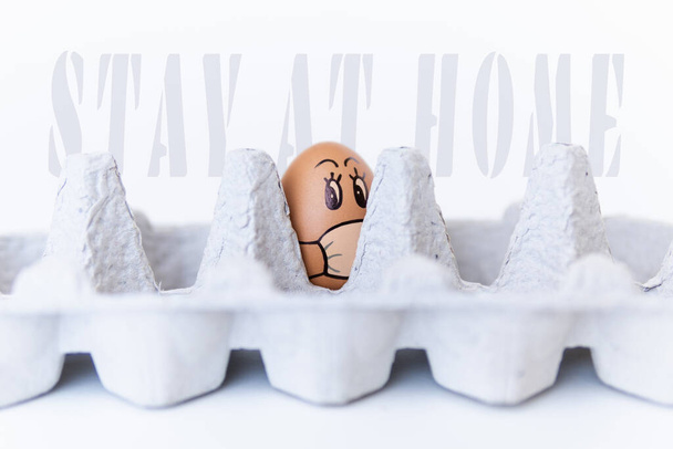 Chicken egg looking out of a tray with doodle face wearing medical mask. Conceptual image of stay at home during Corona virus quarantine - Fotografie, Obrázek