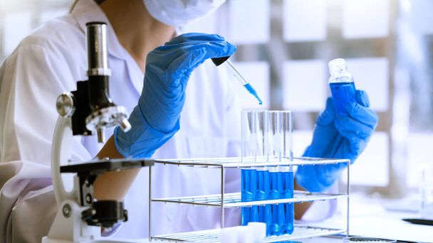 naukowcy badający w laboratorium w białym fartuchu laboratoryjnym, badający rękawice, patrzący na próbkę probówek, koncepcja biotechnologii. - Zdjęcie, obraz