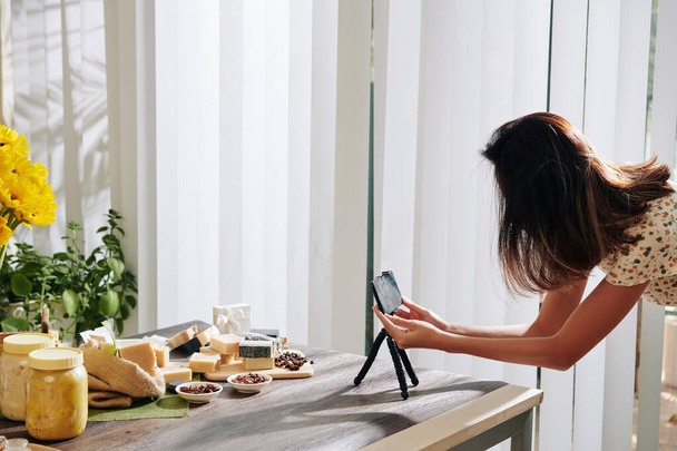 Mujer configuración de teléfono inteligente en trípode y tomar fotos de jabón hecho a mano para su blog o tienda en línea
 - Foto, Imagen