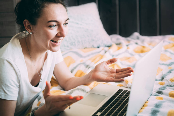 A young woman holds a meeting from home on a laptop. Fun mood. Happy morning Joyful communication with relatives and friends online. Expression of emotions. Stay home concept. Distance communication - Фото, изображение