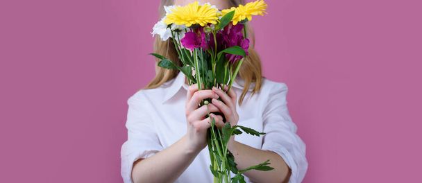 The girl on a pink background holds a beautiful bouquet of different flowers and covers her face. Trend photo without face. - Photo, Image