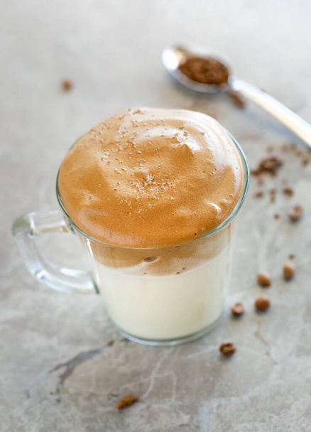 Dalgona Koffie Crème met melk in glazen beker met lepel op de achtergrond - Foto, afbeelding
