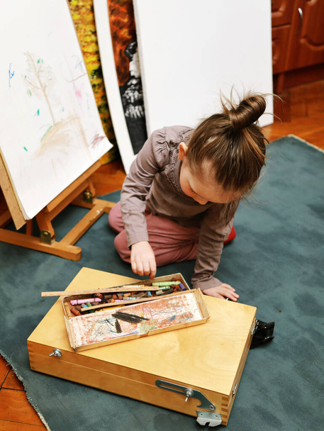 tyttö maalaa maalaustelineeseen pastellilla
 - Valokuva, kuva