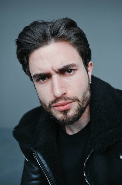 A large portrait of a stylish young man with a beard and dark hair in a black leather jacket - Foto, Bild