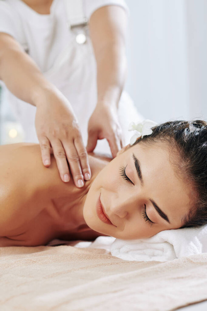 Smiling pretty young woman enjoying shoulder massage in spa salon - Photo, Image
