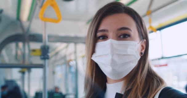 Κοντινό πορτραίτο μιας έξυπνης φοβισμένης φοιτήτριας με ιατρική μάσκα και γάντια που μένει μόνο στα μέσα μαζικής μεταφοράς και κοιτάζει την κάμερα. Το λεωφορείο έχει λίγους επιβάτες.. - Πλάνα, βίντεο