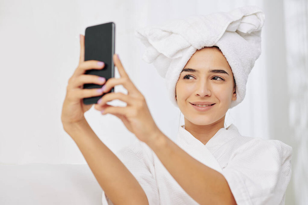 Güzel, genç, gülümseyen bir kadın banyo cübbesi ve kafasında havluyla fotoğraf çekiyor. - Fotoğraf, Görsel