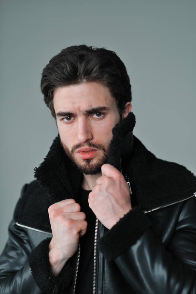 A large portrait of a stylish young man with a beard and dark hair in a black leather jacket - Fotó, kép