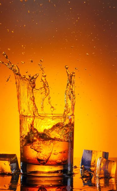 Egy nagy pohár whiskyt permetezéssel lefényképeztek fekete üvegen tükröződéssel. - Fotó, kép