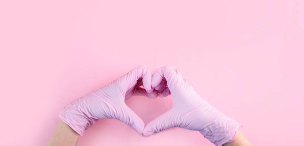 As mãos em luvas médicas são cor-de-rosa na forma de um coração em um fundo rosa com um lugar para texto
. - Foto, Imagem