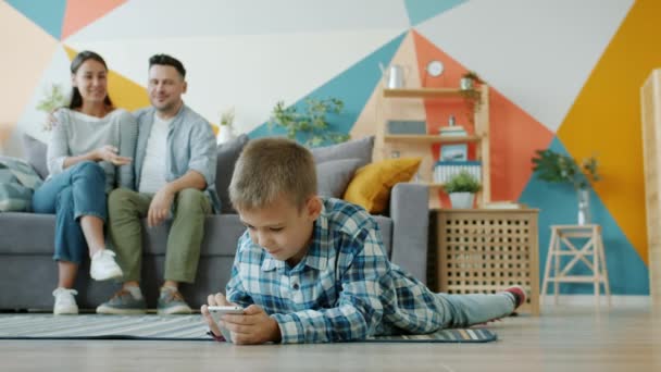 Child using smartphone touching screen while parents watching him talking at home - Filmmaterial, Video