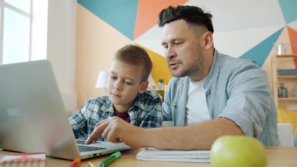 Father and son using laptop for education doing homework smiling in apartment - Materiał filmowy, wideo