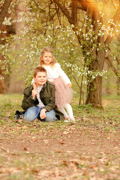 Az őslakos, vidám idősebb testvér és kishúga jól érzik magukat a tavaszi parkban, ahol virágzó cseresznyevirágok vannak egy botanikus kertben. Családi nap. Testvérek napja. Gyermekvédelmi nap. Húsvét - Fotó, kép