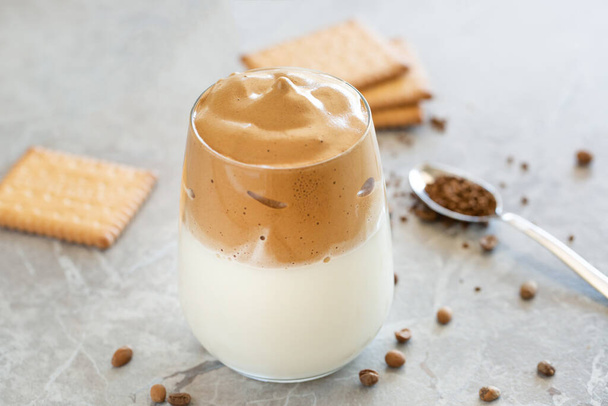 Dalgona Koffie Crème met melk in glazen beker met lepel op de achtergrond - Foto, afbeelding