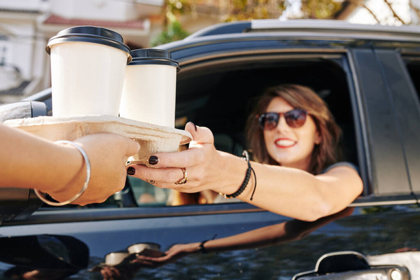 Σερβιτόρος δίνοντας δίσκο μιας χρήσης με δύο φλιτζάνια λάβει έξω καφέ για να όμορφη χαμογελαστή γυναίκα οδηγός - Φωτογραφία, εικόνα