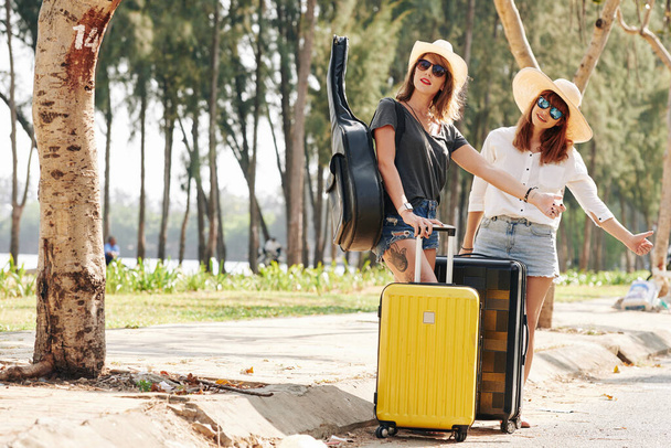 若いです女性旅行者とともにスーツケースとギターキャッチ車上の道路 - 写真・画像