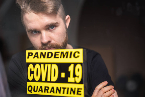 Coronavirus, quarantine, covid-19 and pandemic concept. Sad and sick man of corona virus looking through the window. Stay at home. - Photo, image