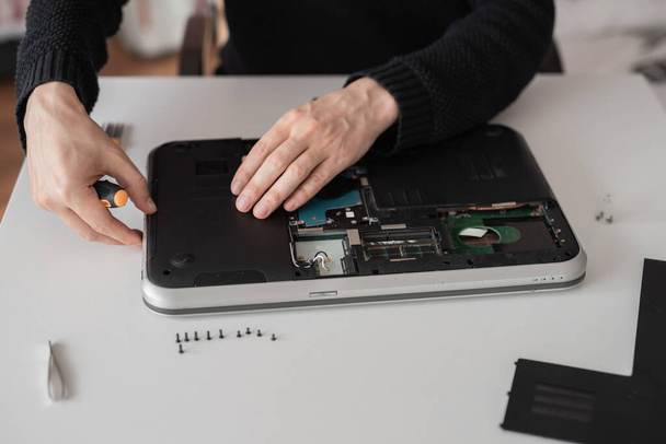 Um homem desmonta um portátil. Serviço de computador e conceito de reparo. Laptop desmontagem na oficina de reparação, close-up. Desenvolvimento eletrônico, fixação de dispositivos eletrônicos
 - Foto, Imagem