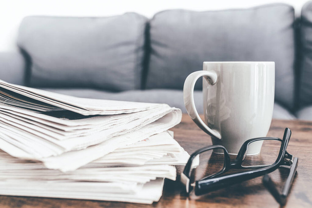 stack of newspapers, coffee mug and glasses on living room table. - Zdjęcie, obraz
