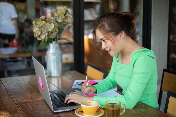 Asijské podnikatelek s úsměvem a pomocí notebooku pro analýzu dokumentů a grafu finanční diagram práce a ona pije kávu - Fotografie, Obrázek