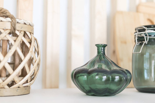 vaso de vidro, jarra e cesta de vime de madeira em um fundo prateleira branca com barras de madeira
 - Foto, Imagem