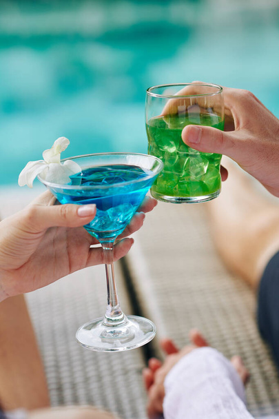 Couple cliquetis avec des cocktails colorés doux lors du repos près de la piscine
 - Photo, image