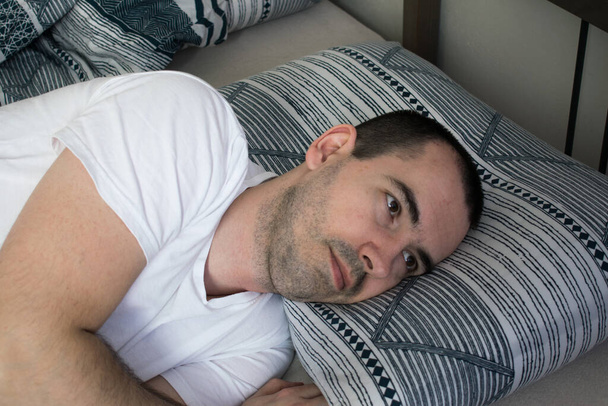 férfi fekszik az ágyon párna nyitott szemmel, nem tud aludni. Álmatlanság. Tünetek és okok. Alvási nehézség. Annak a jele, hogy rossz az alvásminőséged. Rendellenességek és problémák. Alvászavar okai, diagnózis - Fotó, kép
