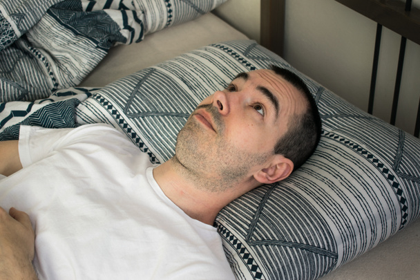 男のベッドの枕を開いて目には、眠ることができないうそ。不眠症.症状と原因.睡眠の難しさ。睡眠の質が悪いという兆候。障害と問題。睡眠障害,診断 - 写真・画像