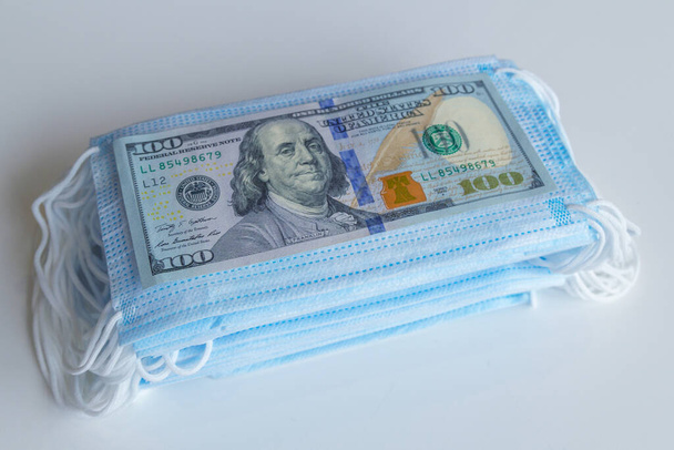 paczkę masek medycznych i stos banknotów 100 dolarów jako symbol wyższych cen i niedoboru ochrony dróg oddechowych przed wirusami. Zwiększono cenę masek ochronnych. - Zdjęcie, obraz