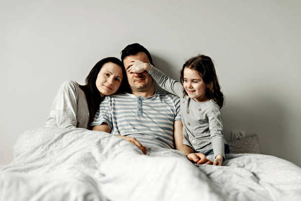 portrait of a young family in bed,happy father and mother lie with their daughter in bed in the early morning,young family hugs tightly,positive morning in a happy family - Photo, image