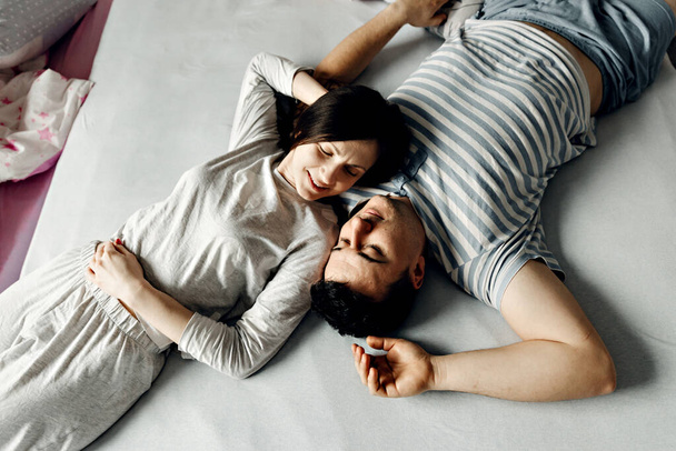 couple in love in bed,happy young family wakes up early in the morning in bed,top view of a couple who wakes up,husband and wife are smiling and hugging tenderly,peeping on the couple who is on the bed - Foto, immagini
