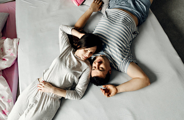 couple in love in bed,happy young family wakes up early in the morning in bed,top view of a couple who wakes up,husband and wife are smiling and hugging tenderly,peeping on the couple who is on the bed - Foto, Imagen