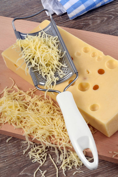 Целый и тертый сыр на разделочной доске с теркой для сыра
 - Фото, изображение