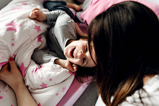 μητέρα με κόρη το πρωί, νεαρή μητέρα βρίσκεται στο πάτωμα με την κόρη της τυλιγμένη σε μια κουβέρτα, ευτυχισμένη μαμά θαυμάζει την κόρη, σχέση της κόρης με τη μαμά - Φωτογραφία, εικόνα