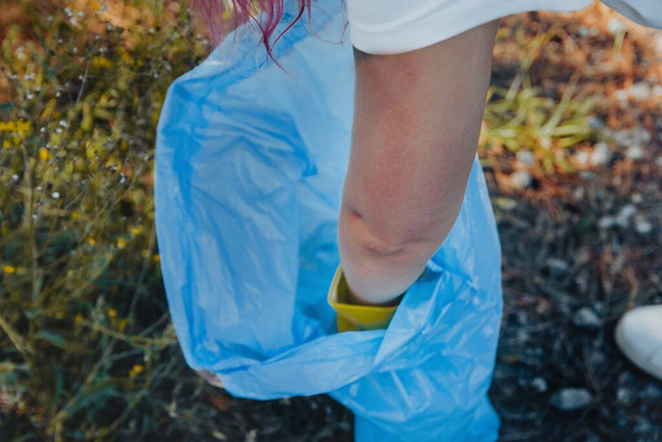 A young female collecting the trash and putting in a plastic garbage bag - environmental pollution concept - Zdjęcie, obraz
