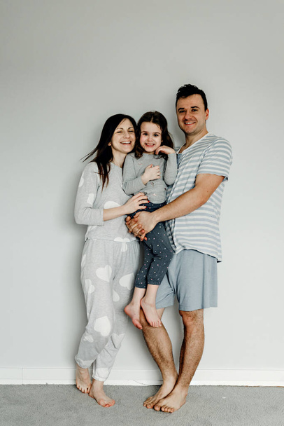 portret van een gelukkig gezin in de ochtend, familie in pyjama 's, familiefoto, gelukkig jong gezin poseren in pyjama' s voor de camera, vader, moeder en dochter nemen een foto als aandenken - Foto, afbeelding