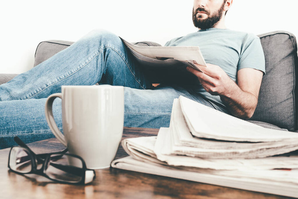 hombre relajándose en el sofá leyendo un periódico
 - Foto, Imagen