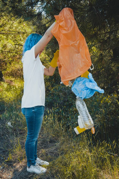 A young female collecting the trash and putting in a plastic garbage bag - environmental pollution concept - Фото, изображение