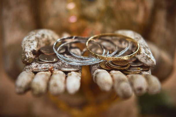 A closeup of bracelets and coins in the hands of the Buddhist guardian statue in Pha Lat Temple - Valokuva, kuva