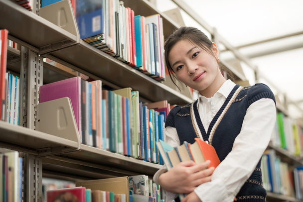 Student holding books next to bookshelf - Photo, Image
